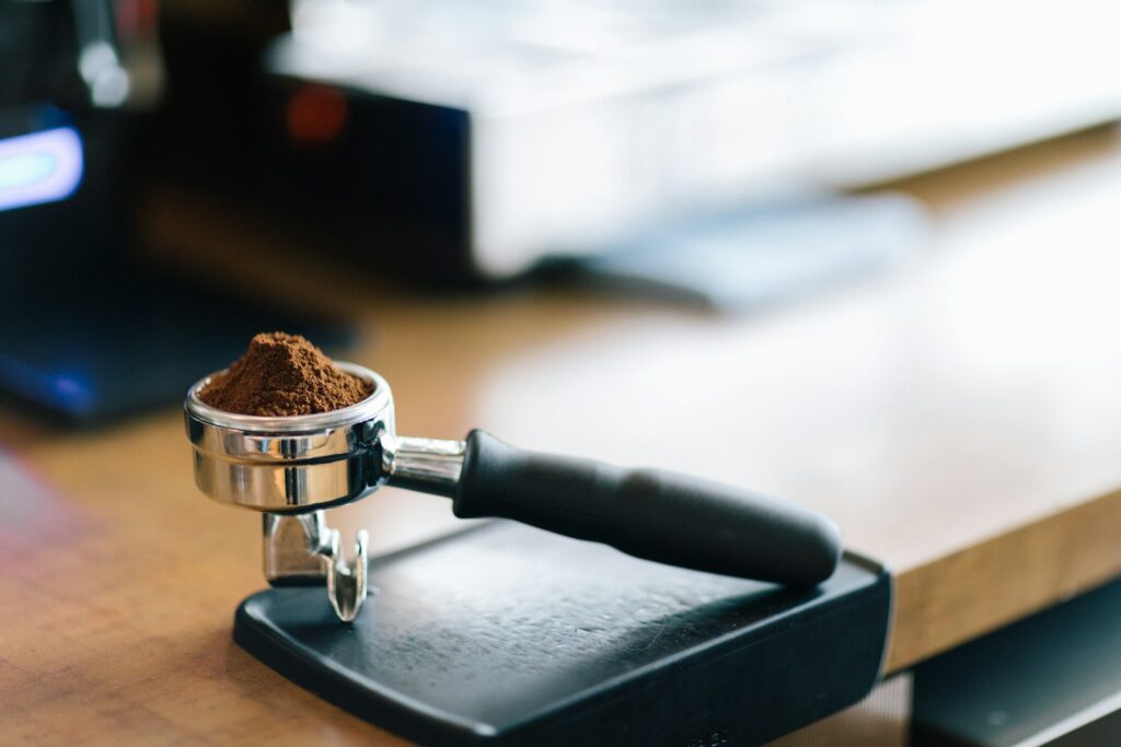 Portafilter met verdeelde koffie naast een espressoweegschaal en tamper
