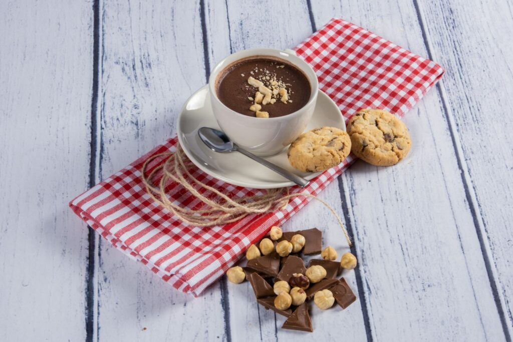 Kop koffie met melk naast hazelnoten en stukjes chocolade